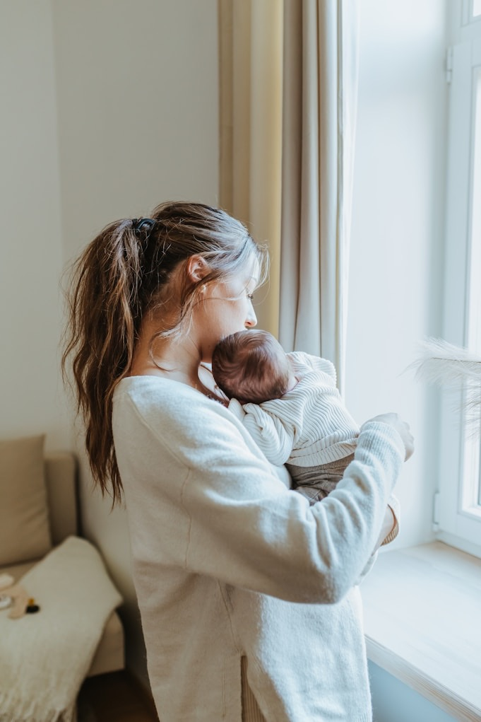 A parent holding their baby by a window